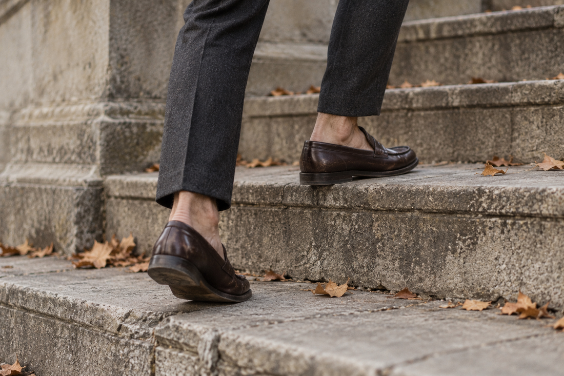 A man in cropped trousers and brown penny loafers walking up stone steps with no socks showing