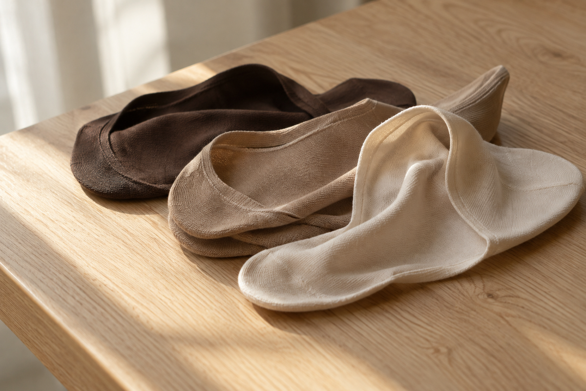 Thin no show socks in brown, tan and white resting on an oak table in soft morning light
