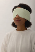 Woman wearing the Deep Rest Sleep Mask in Honeydew Green, which wraps across her eyes